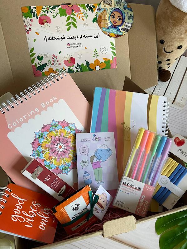 عکس باکس هدیه عاطاباکس مامان پلاس مدل رنگی باش شامل دفتر رنگ‌آمیزی ماندالا، پلنر پیتیکو، روان‌نویس‌های نئونی، دفترچه Good Vibes Only، کش‌سر شش‌تایی، بالم لب ثمین، استیکر آب زیاد بخور و پک چای میوه‌ای چهارطعم با تم نارنجی–گلبهی.