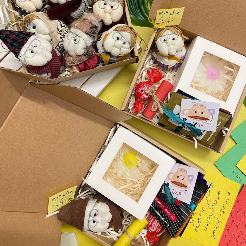 یلداباکس بسته هدیه شب یلدا شامل عروسک پارچه‌ای دست‌ساز مادربزرگ یا پدربزرگ، شعر حافظ، شمع بابونه، چای میوه‌ای و شکلات
