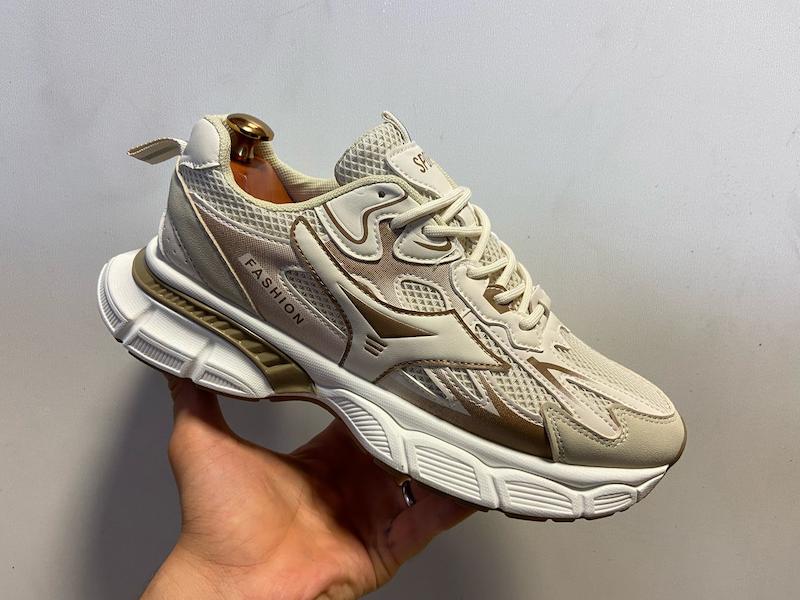  کتونی اسپرت مردانه کرم با رویه مشبک تقویت‌شده، پنل‌های لایه‌کاری شده حرارتی، لوگوی جانبی برجسته، زیره طبی حجیم مخصوص استفاده روزمره و پیاده‌روی؛ نمایش جزئیات کامل از زاویه کناری کفش