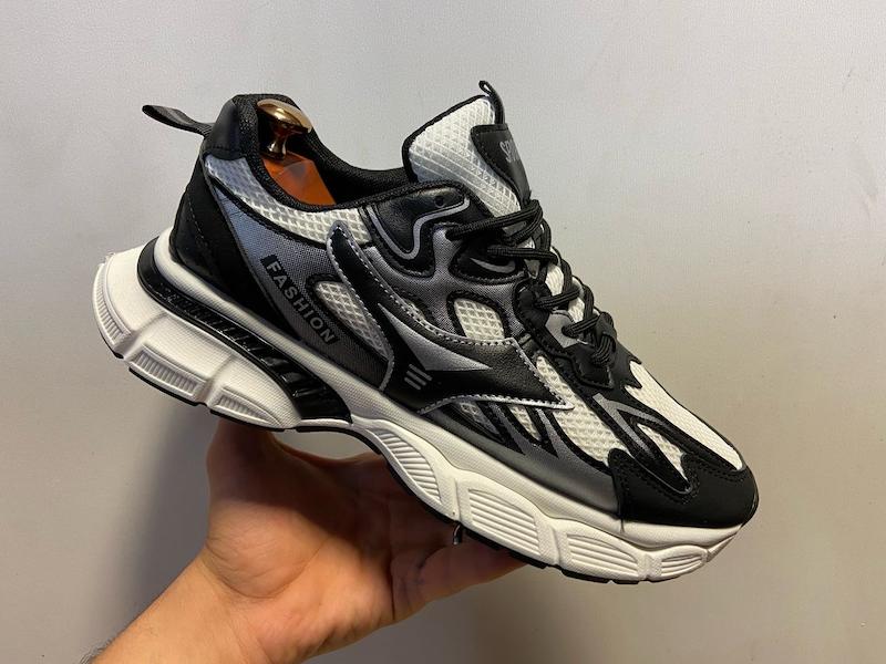  کتونی اسپرت مردانه مشکی سفید با طراحی تهاجمی، رویه مشبک دوبل، پنل‌های چرمی تقویت‌شده، زیره حجیم با خطوط اسپرت؛ عکس از نمای کناری با نمایش کامل جزئیات ساختار کفش