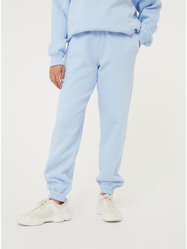 شلوار اسلش زنانه لایت‌بلو با فیت راحت و دم‌پا کشی، تن‌خور آزاد و اسپرت، همراه با جزئیات مینیمال و لوگوی ظریف روی ران، ست‌شده با سویشرت همرنگ و کتانی سفید – BAZARELL