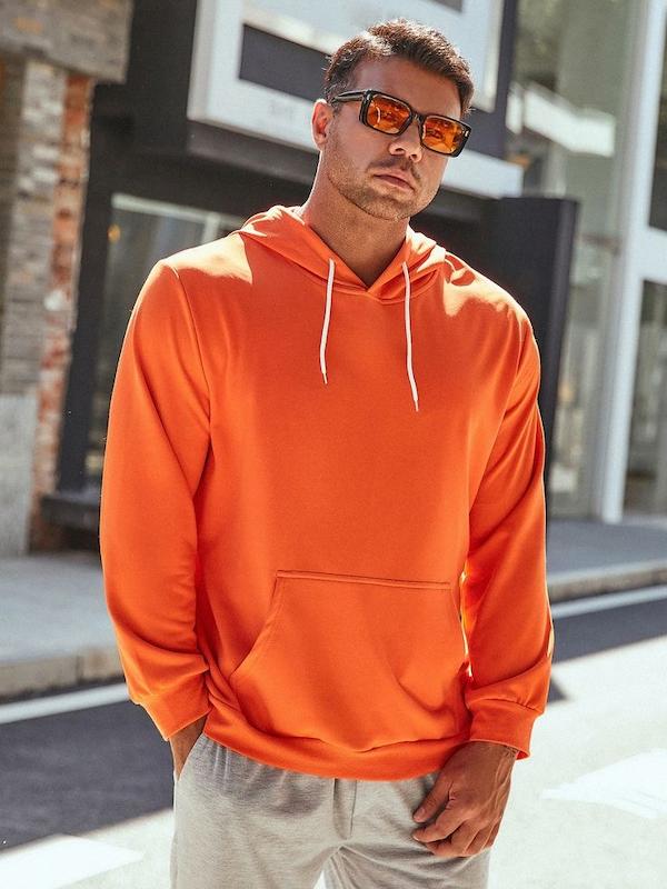 هودی مردانه نارنجی رنگ با جنس ضخیم و کلاه‌دار، مناسب استایل خیابانی، تنخور آزاد، دارای جیب کانگورویی و بند سفید.