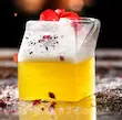 لیوان شیشه‌ای دوجداره طرح پاکت شیر با دسر زرد و خامه توت قرمز روی سطح شیشه‌ای