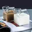 دو لیوان شیشه‌ای دوجداره طرح پاکت شیر یکی با قهوه و دیگری با شیر، کنار میز کار