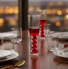 لیوان شیشه‌ای دوجداره طراحی موج‌دار منحنی برند Perotti با نوشیدنی قرمز روی میز چوبی چیدمان شده