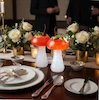 دو لیوان شیشه‌ای طرح قارچ با نوشیدنی قرمز، چیدمان‌شده روی میز شام مجلسی با گل‌های سفید