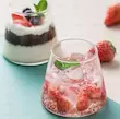 لیوان شیشه‌ای مدرن مخروطی با نوشیدنی خنک و تکه‌های توت‌فرنگی، برگ نعنا و یخ، روی پس‌زمینه آبی