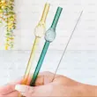 دست در حال نگه داشتن نی شیشه‌ای سبز و طلایی با جزئیات گل شیشه‌ای