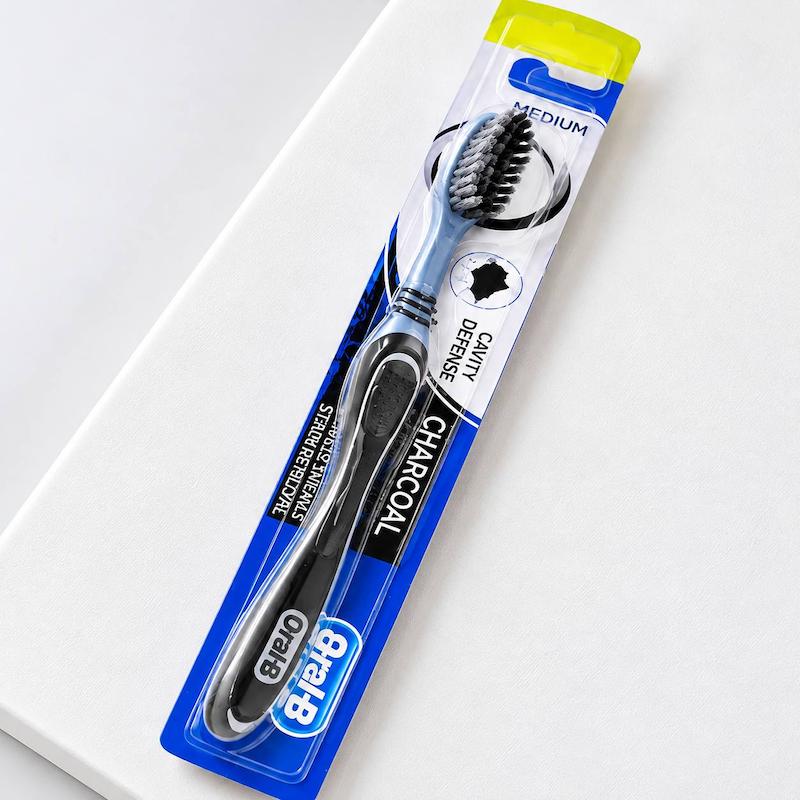 نمای کامل مسواک Oral-B Charcoal برس متوسط در بسته‌بندی آبی و شفاف با عنوان Medium