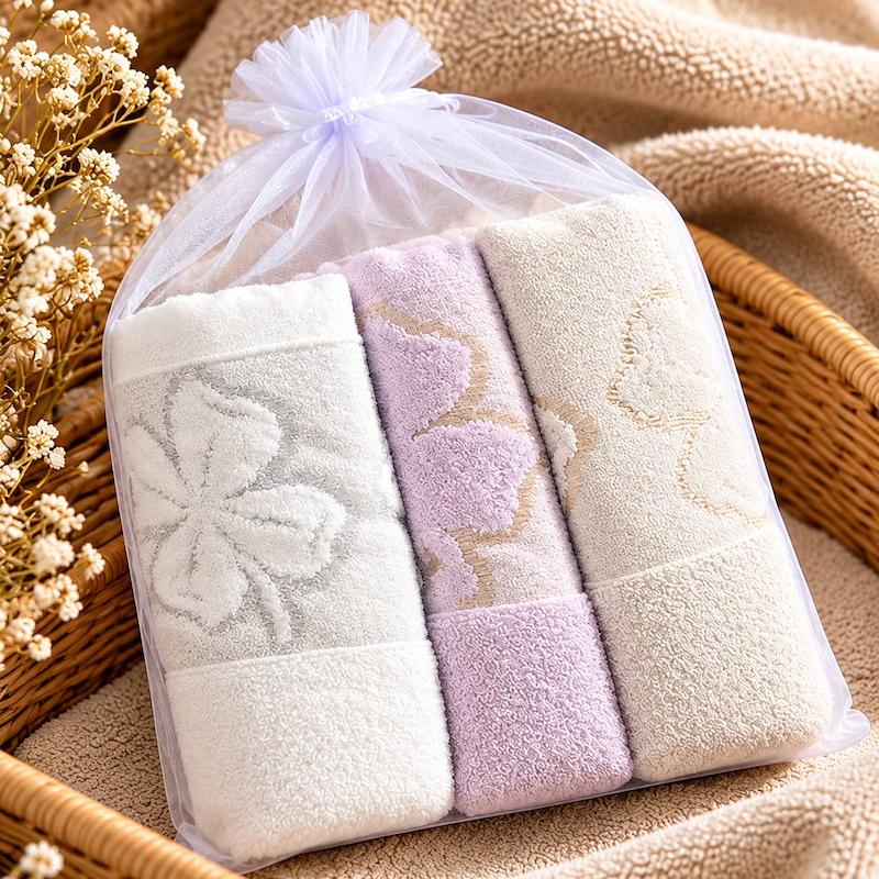 نمای روبه‌رو از سه حوله گل‌دار با بافت حلقه‌ای و رنگ‌های ملایم در بسته‌بندی توری بنددار