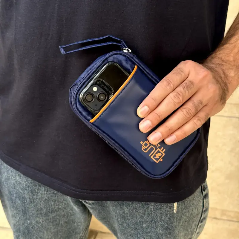 کیف لوازم دیجیتال سرمه‌ای در دست مرد به همراه گوشی موبایل