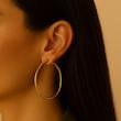 گوشواره حلقه‌ای ساده طلایی سایز بزرگ روی گوش مدل زنانه با زمینه کرم