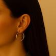 گوشواره حلقه‌ای طلایی سایز متوسط استیل روی گوش مدل زنانه با پس‌زمینه کرم