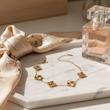 دستبند ونکلیف تراش‌خورده طلایی کنار عطر و روسری بژ روی میز مرمر