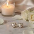گوشواره قلب صدفی در کنار شمع و گل‌های سفید روی سنگ مرمر