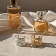 دو انگشتر بنگلی استیل طلایی و نقره‌ای روی میز مرمری کنار عطر