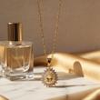 گردنبند طلایی نگینی کنار شیشه عطر طلایی و پارچه براق