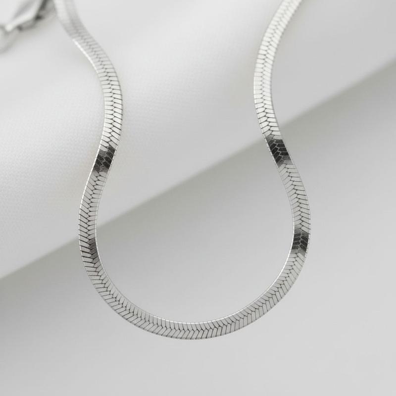 نمای نزدیک زنجیر نقره‌ای تخت روی پارچه سفید