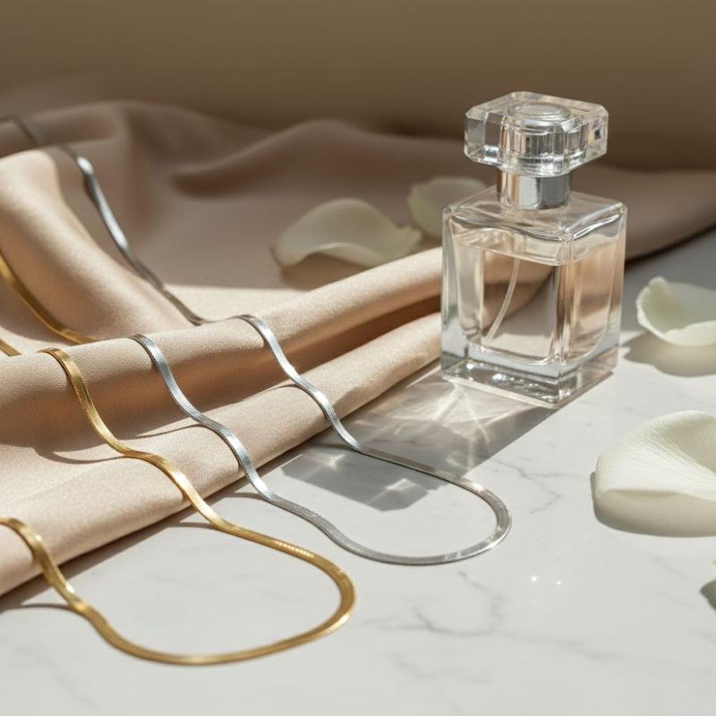 زنجیرهای طلایی و نقره‌ای هرینگبون کنار شیشه عطر و گلبرگ‌ها در نور آفتاب