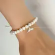 دستبند مروارید طبیعی با پلاک نقره عیار ۹۲۵ طرح دم وال و قفل کشویی نقره نلیسا روی دست مدل با زمینه سفید