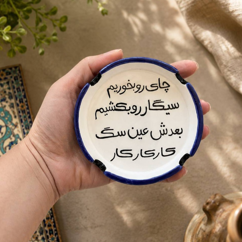 زیرسیگاری سرامیکی دست‌ساز با نوشته چای رو بخوریم سیگار رو بکشیم بعدش عین سگ کار کار کار