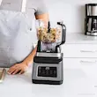 غذاساز نینجا مدل BN801 با مخلوط‌کن بزرگ پر از میوه و ظرف غذاساز پر از خمیر کوکی در یک آشپزخانه مرتب و روشن قرار دارد.