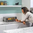 خانمی در حال مشاهده غذای در حال پخت داخل آون توستر نینجا مدل SP101.