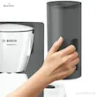 دستی در حال جدا کردن مخزن آب خاکستری شفاف و مدرج قهوه ساز بوش مدل TKA6A041 از بدنه دستگاه.