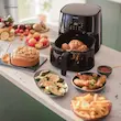 سرخ کن بدون روغن فیلیپس مدل HD9270 مشکی در آشپزخانه، در کنار میز بزرگی پر از غذاهای متنوع پخته شده. 