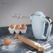 همزن برقی دستی اسمگ مدل HMF01 آبی پاستلی با سری خمیرزن روی میز آردپاشی شده.