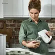 یک زن در حال استفاده از همزن دستی برقی کنوود مدل HMP30 سفید در یک کاسه شیشه ای کوچک.