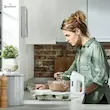یک زن در آشپزخانه در حال خواندن کتاب دستور پخت در کنار همزن دستی برقی کنوود مدل HMP30.