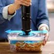 یک دست در حال استفاده از پمپ وکیوم گوشت کوب برقی بوش مدل MS6CB61V1 روی ظرف نگهدارنده غذا.