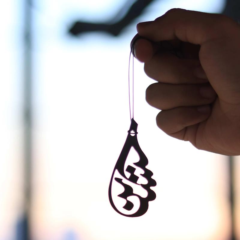 نمای نزدیک از ابعاد واقعی آویز آینه خودرو استیل طرح حسین با تایپوگرافی هنری در دست کاربر