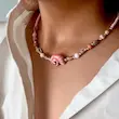 گردنبند چوکر منجوقی صورتی با صدف حلزون و مهره‌های طلایی روی گردن مدل