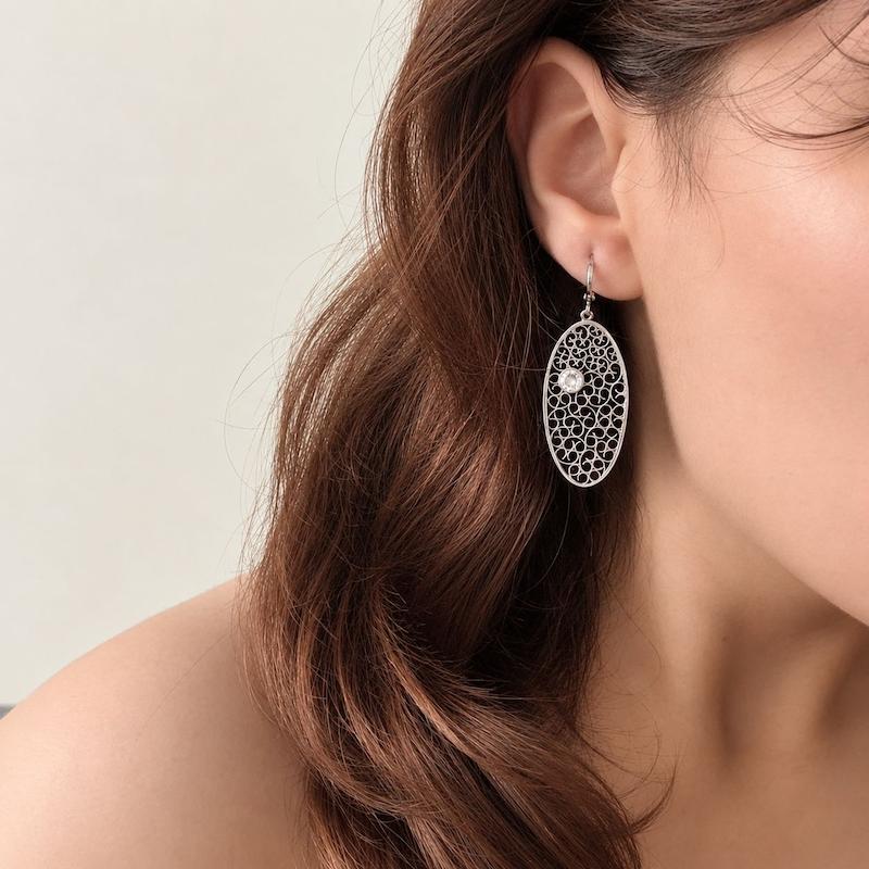 گوشواره آویز بیضی نقره‌ای با طرح اسلیمی و نگین مرکزی روی گوش