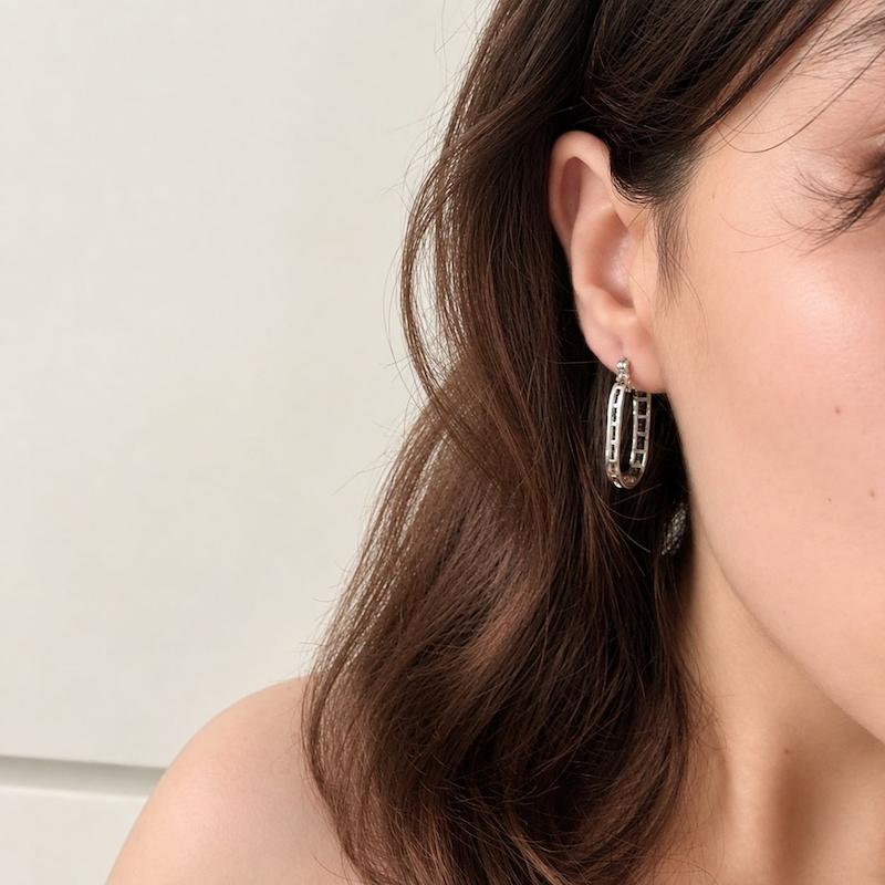 گوشواره حلقه‌ای بیضی نقره‌ای با جزئیات مستطیلی روی گوش زن